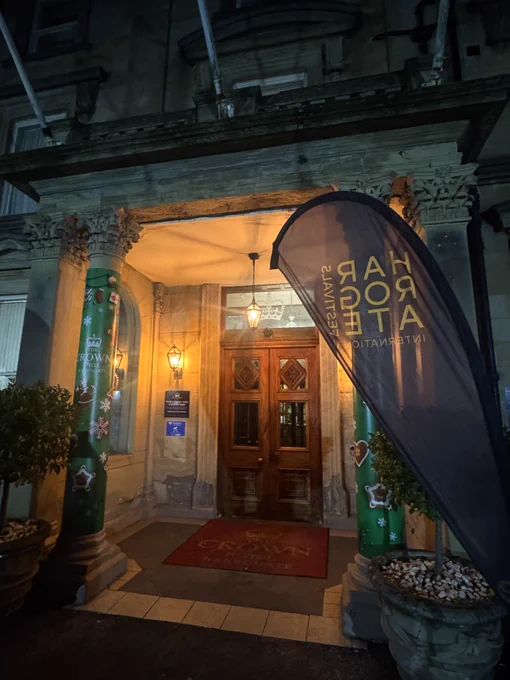 Nighttime hotel entrance with ornate columns, holiday decorations, and warm lighting. "Crown Hotel" text on red mat. Vertical banner nearby.
