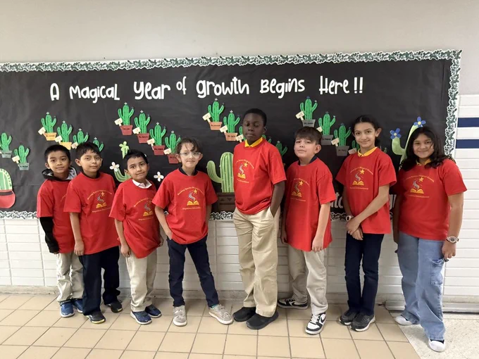8 students posing with their shirts that say "reading sparks magical growth"