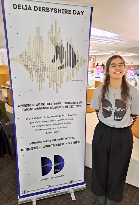 Young woman smiling next to Delia Derbyshire Day poster 