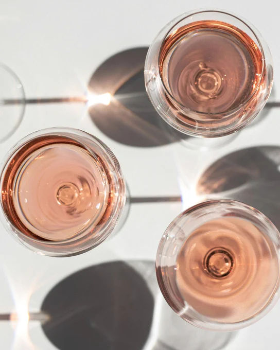 Top view of three glasses of rosé wine casting circular shadows on a light surface.