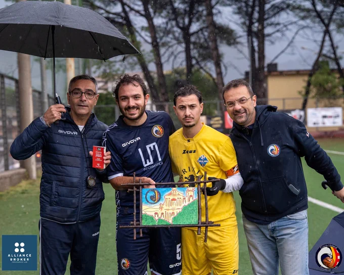 Cava United players and staff on the field in the rain, holding a literary “figurina” about the Jaber brothers and a handmade artwork — symbol of the club’s community-driven model of sport.