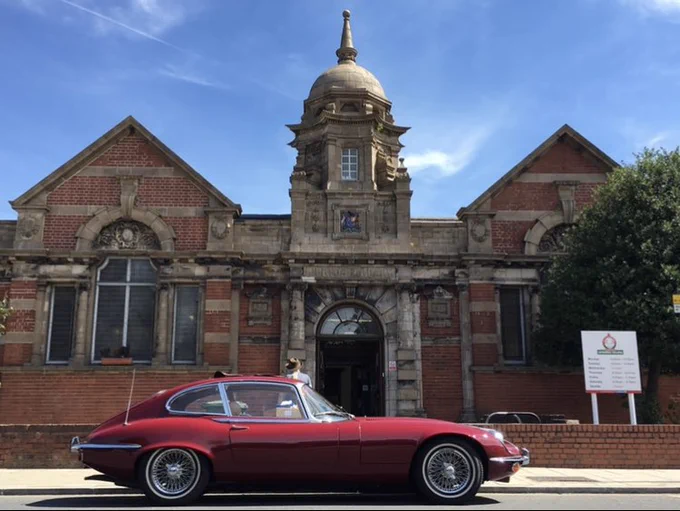 Photo by Paul de Zylva, library volunteer, of a red Jaguar E-type on the road in front of the Corbett Community Library, known to many as Torridon Library on the junction of Torridon Road and Sandhurst Road in Catford, Lewisham, London, SE6.