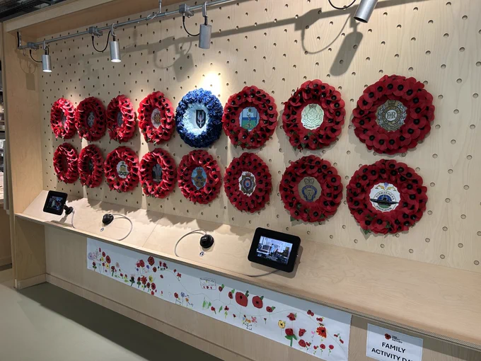 A selection of Poppy wreaths with different regimental badges at their centre. These are displayed along a wall.
