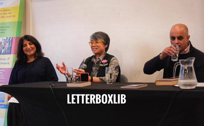 Panel. Left is Gita Ralleigh, laughing. Middle is Candy Gourlay who is speaking; expressive hands. Right is Bali Rai drinking a glass of water.