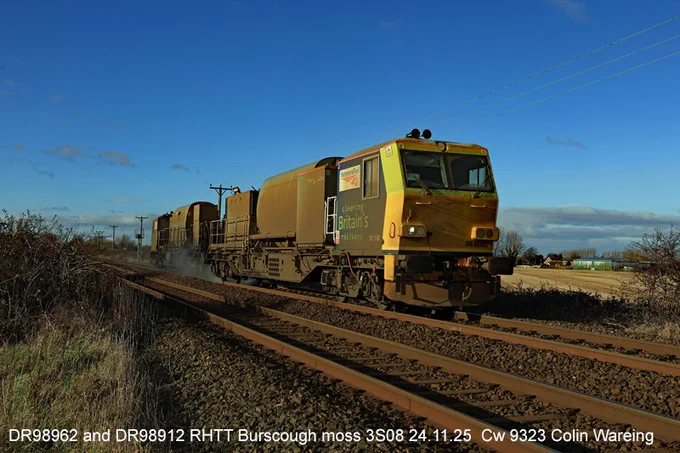 Cw 9323 DR98962 and DR98912 RHTT Burscough moss 3S08 24.11.25 
Network rail MPV no DR 98962 approaches the pedestrian foot crossing between the station at New Lane and Burscough Bridge station in West Lancashire working a rail head treatment train on Monday afternoon the 24.11.25.
DR 98912 is paired with her sister unit DR 98912 the pair having set off from the depot near Wigan at 03.15 hrs this morning on railhead treatment working visiting various lines in the northwest before arriving back in Wigan at 13.40 hrs this afternoon.
The train is spraying a high-power jet of water at the top of the rails to remove the build up of fallen leaves and applying an adhesion paste to reduce wheel adhesion problems for the trains and rail industry at this time of the year.
The date is 24.11.25	
Image Cw 9323 copyright Colin Wareing of Colin and Carole’s Creations

