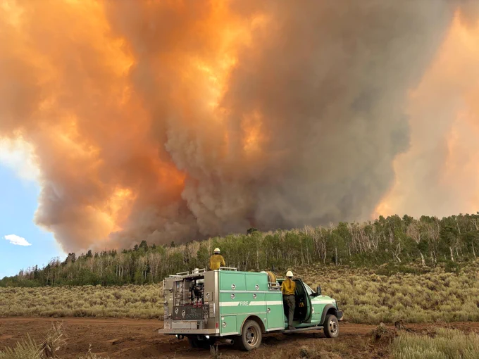 Monroe Canyon Fire, Utah. Wildland firefighters stand on their Forest Service engine and observe the plume of smoke from a wildfire in the distance. 