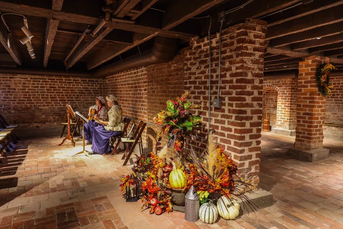 Musicians playing in the Francis Land House cellar near some fall/Thanksgiving decorations.