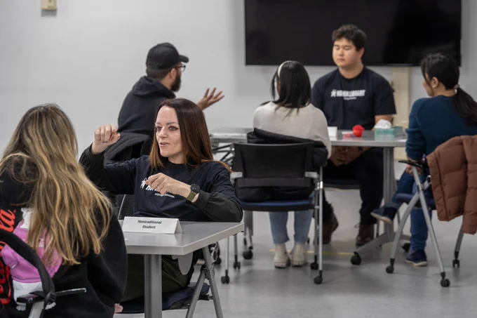 Group of people engaged in discussion around tables in a classroom setting.