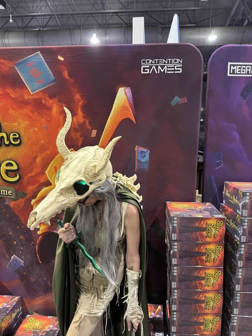 A silent cosplayer posing in front of the slay the spire booth with her dagger. The skull eye sockets are glowing green.