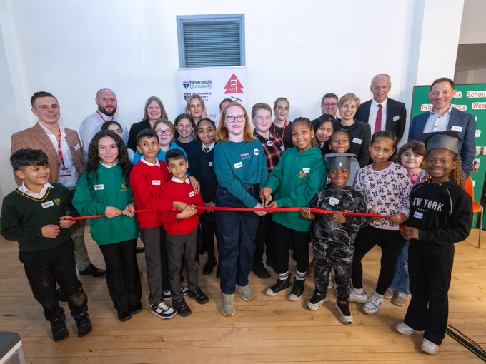 Group of diverse children and several adults participating in a ribbon-cutting ceremony at an event.
