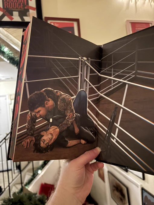 One of the endpapers, showing a man in camo trapping the protagonist against the ground in a livestock auction lot (no animals), and holding his face. There is a shotgun leaning against the bars.