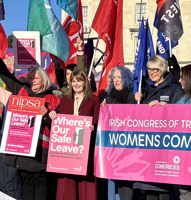 Women, including Economy Minister Dr Caoimhe Archibald, at Stormont, holding banners to support workers who are victims and survivors  of domestic abuse.