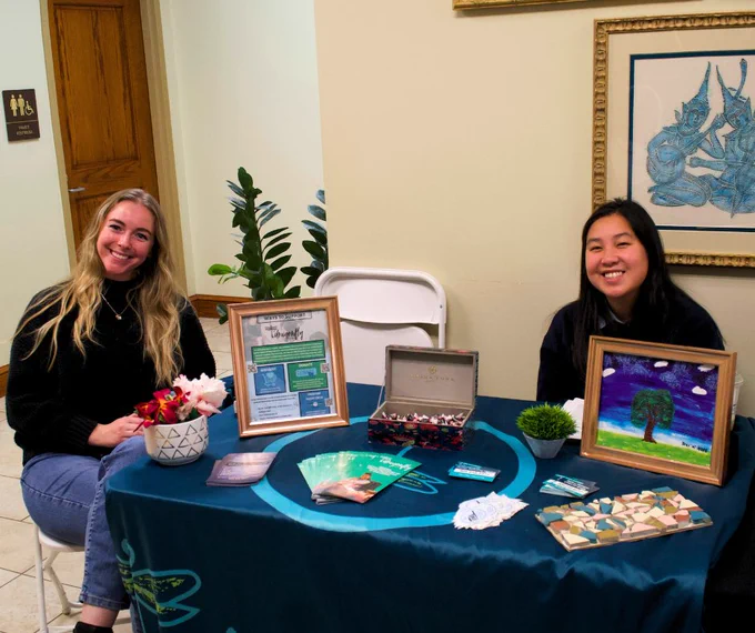 Two people sitting at a table displaying various art pieces and promotional materials.