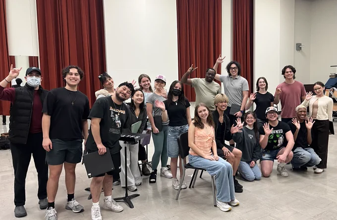 Group of people smiling and posing in various playful gestures in a rehearsal room.