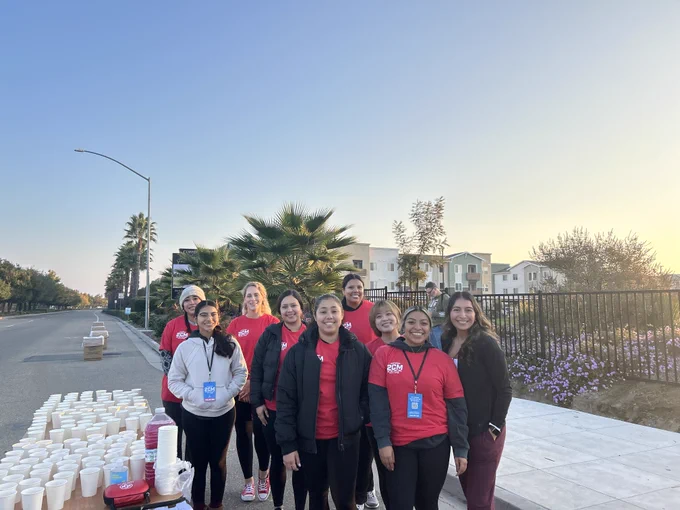 Group of volunteers wearing red shirts standing on a sidewalk, with trays of water.