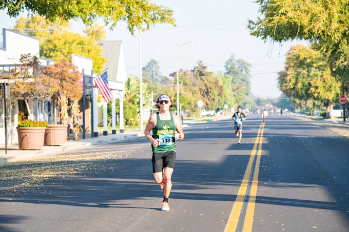 Dr. Steven Waite running in a marathon on a sunny street lined with American flags and trees.