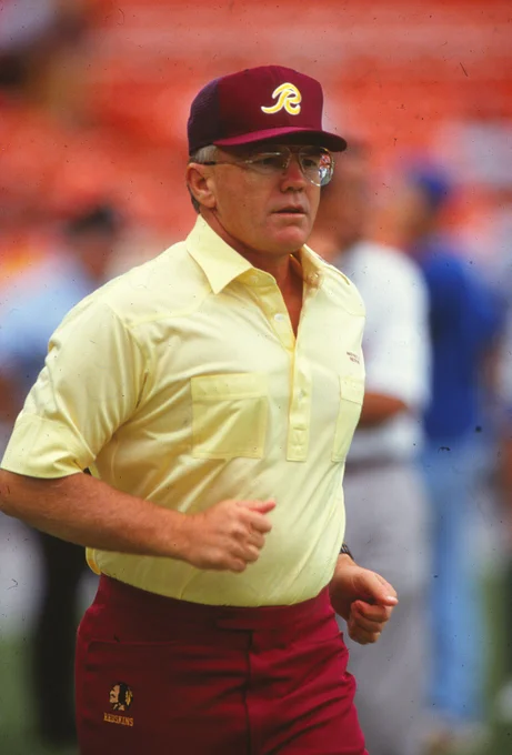 Photo of Joe Gibbs. He is wearing a burgundy hat, gold shirt and burgundy pants.