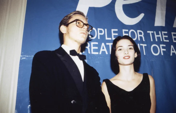 Winona Ryder and River Phoenix stand in front of a large blue PETA banner.