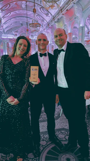 three people in black tie attire pose with an award