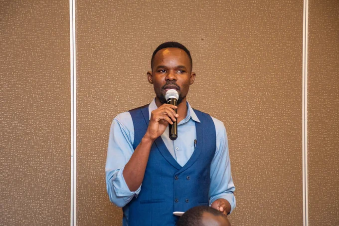 A pic of myself in a light blue shirt with a navy blue halfcoat. I am holding a microphone