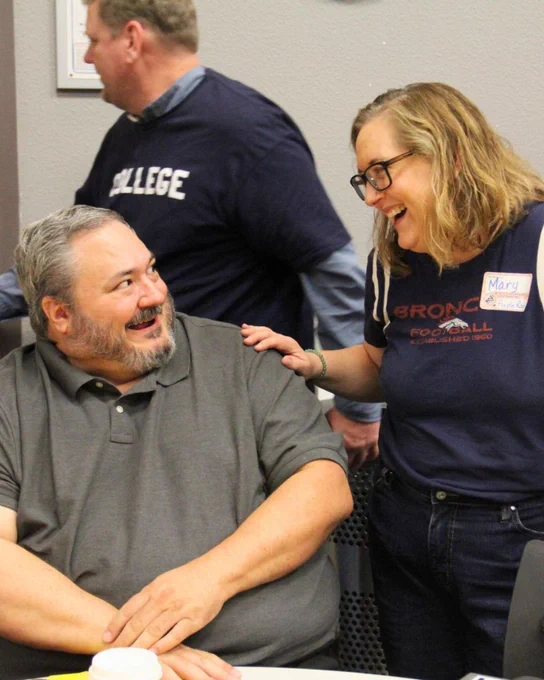 Two individuals, one wearing a "Mary" name tag, sharing a joyful moment at a social gathering.
