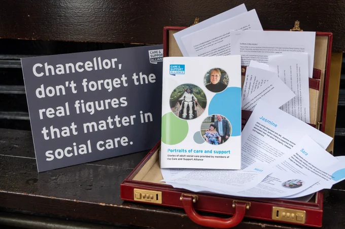 Photo of a red briefcase, open, filled with stories, letters and notes from older people, disabled people and unpaid carers. A sign next to it reads 'Chancellor, don't forget the real figures that matter in social care.'