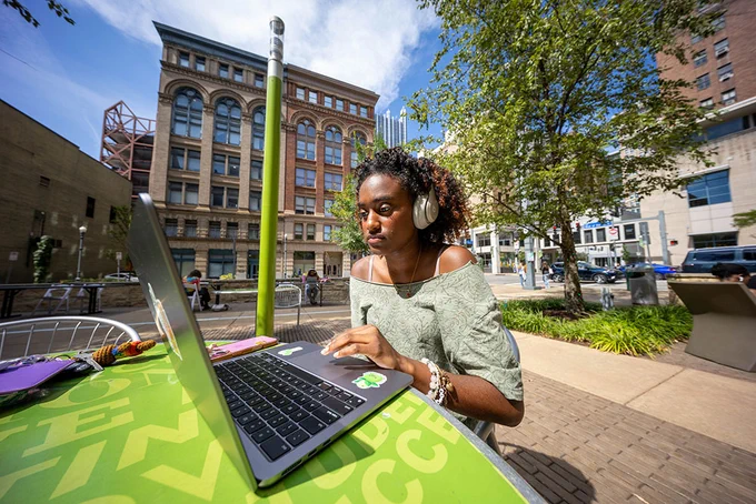 Person using a laptop at an outdoor table in an urban setting.