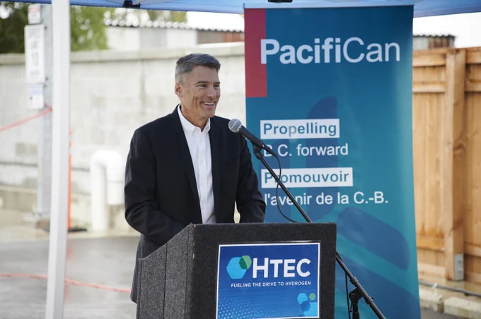 Minister Gregor Robertson standing at a podium with a PacifiCan banner in the background and an HTEC logo on the podium.