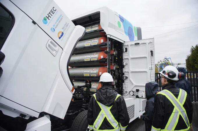 Un groupe de personnes debout à côté d’un gros camion portant le logo HTEC.