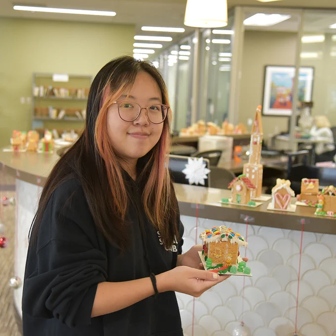 Student holding a mini gingerbread house in Payson Library.