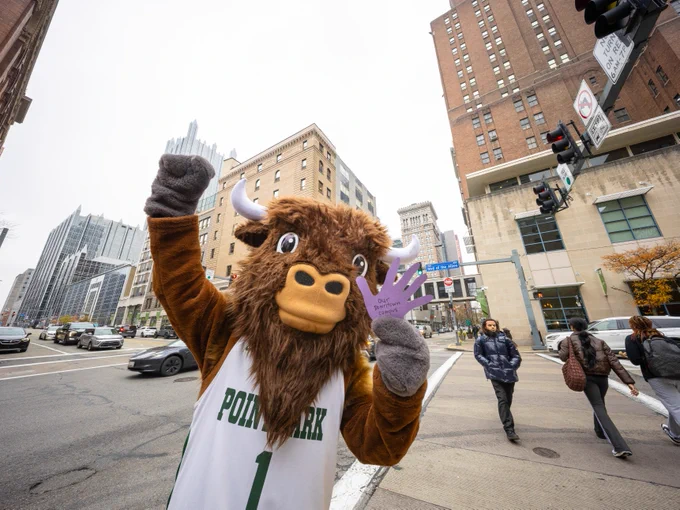 Black Diamond II, Point Park University's mascot, holding up a thankful hand in the middle of campus with the city of Pittsburgh in the background.