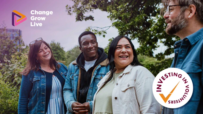 Four diverse volunteers standing outdoors in a park, engaged in friendly conversation under leafy trees during daytime.