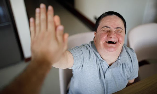Man with learning disabilities puts hands up to another's.  Man has missing teeth. Aims to illustrate article about improving oral health of people with learning disabilities and what nurses can do to help this.