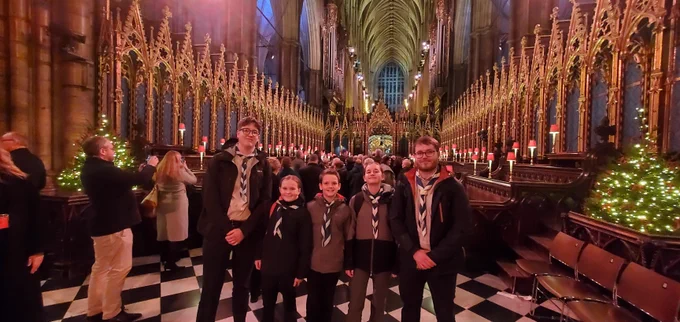 Interior of Westminster Abbey during a festive celebration with Scouts standing in the aisle, surrounded by lit candles and Christmas trees.