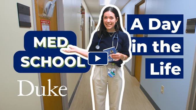 A medical student stands in a corridor, wearing a stethoscope and holding a card. Text overlays include "MED SCHOOL," "A Day in the Life," and "Duke." The setting features beige walls and multiple doors. A play button indicates video content.