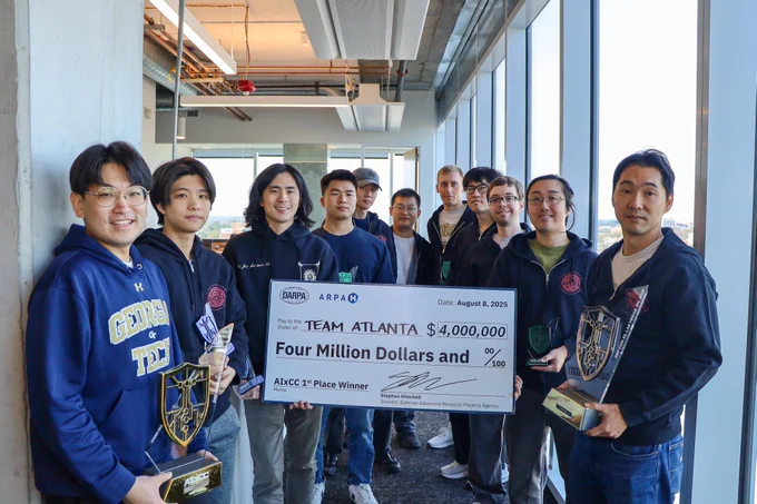 A small group of Team Atlanta members stand with their trophies in the School of Cybersecurity and Privacy. In the center the team holds a large cardboard check that reads, Team Atlanta, Four Million Dollars.