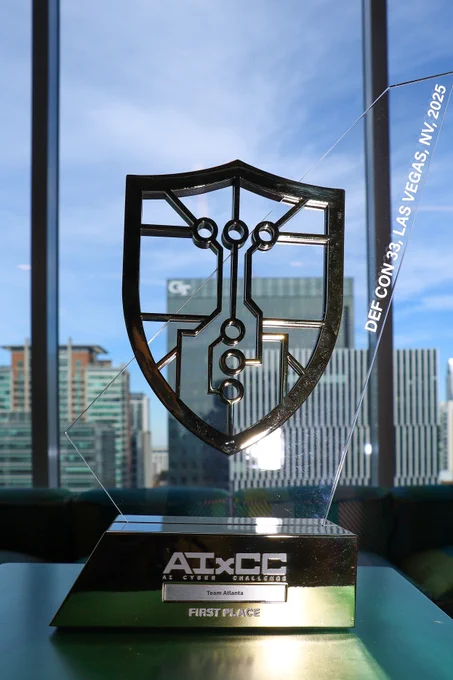 A trophy in front of a window. Behind it there are city buildings, including one with a GT on it. The trophy says, AIxCC First Place Team Atlanta. Def Con 33, Las Vegas.