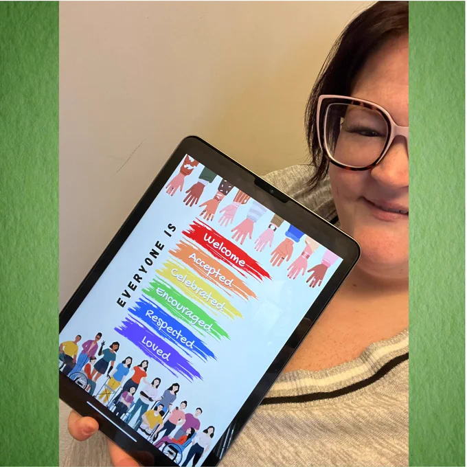 A partially visible person holds an iPad with a graphic that has a row of open hands at the top and a row of many illustrated people across the bottom. Stripes in rainbow colors read, “Everyone is welcome, accepted, celebrated, encouraged, respected, loved.”