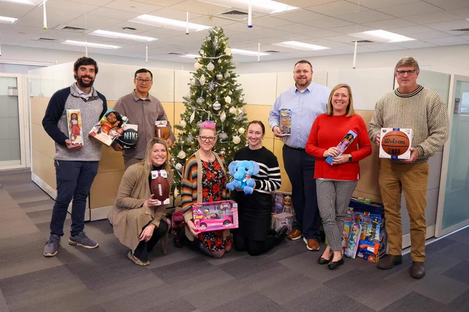 Group of UVA Facilities Management employees in an office holding various toys with a Christmas tree in the background.