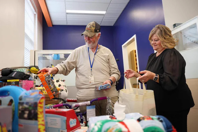 Two UVA Facilities Management employees hold toys, with various other toys and games visible on the shelves around them.