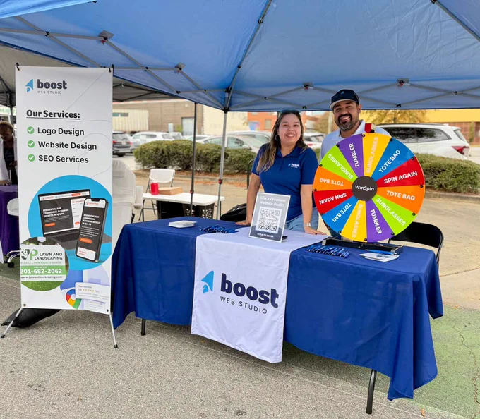 Kim and Manny at the Boost Web Studio vendor table with colorful spinning wheel on top of table.