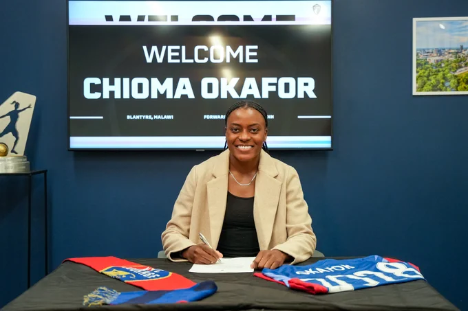 Chioma Okafor smiles signing a contract with welcome graphic on the screen behind her