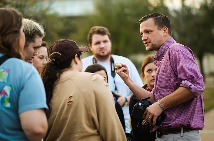 Man speaks to a group of students in an outdoor setting. 