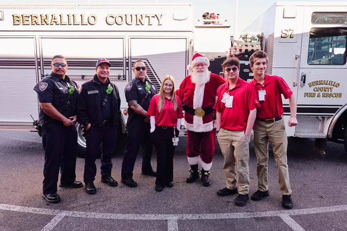 Group of people, including police officers and Santa Claus, standing next to a Bernalillo County Fire & Rescue vehicle.