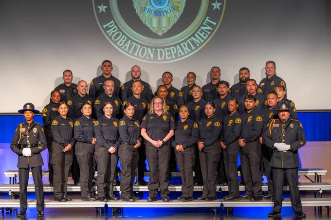 A group of probation officers posing together for a graduation celebration photo, with the Chief Probation Officer and honor guard.