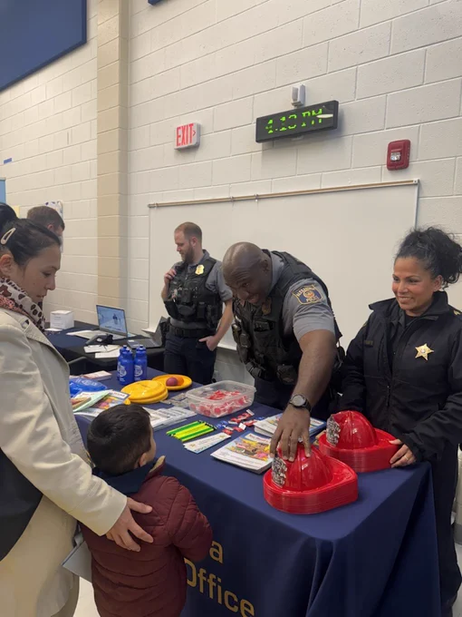 Community members interacting with law enforcement officers at an indoor event, with educational materials displayed on a table.