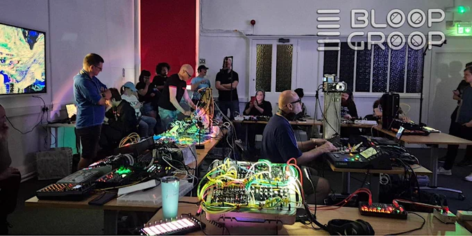 A group of people engaged in a live electronic music jam session, surrounded by synthesizers and cables. The text "Bloop Groop" is visible in the forefront of the photo.
