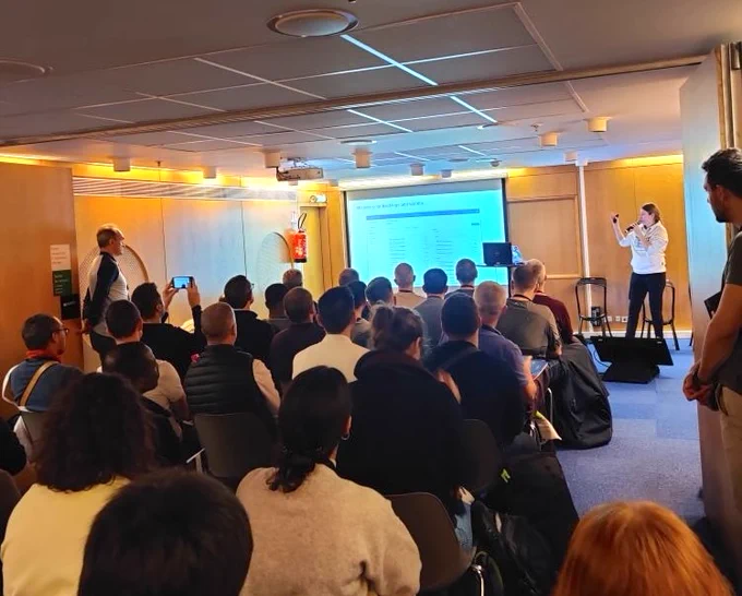 Rosanna Sibora giving a presentation at OSXP 2025 to a full room, speaking in front of a projected slide on project and knowledge management.