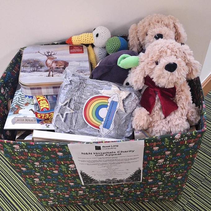 A box wrapped in Christmas wrapping paper full of toys, biscuits, chocolates and toys. A sign on the front reads N&N Hospitals Charity Gift Appeal.