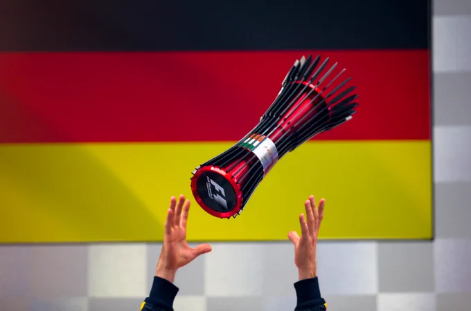 Sebastian Vettel throws his 2013 Indian GP trophy in the air, with the German flag displayed in the background.